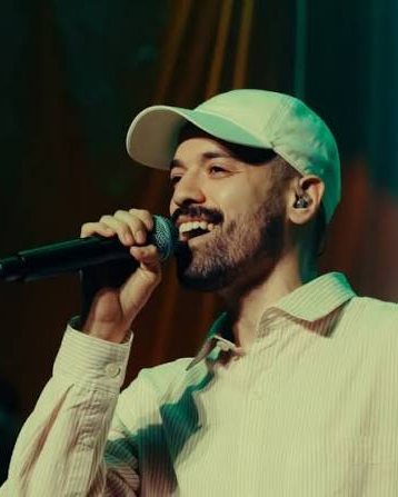 Caetano cantando no palco, de boné branco